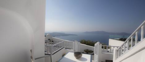 Una terrazza esterna bianca con tavolo e sedie, affacciata su una vista panoramica del mare e isole in lontananza.