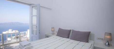 A bedroom with a bed, pillows, bedside tables, and a view of the sea.