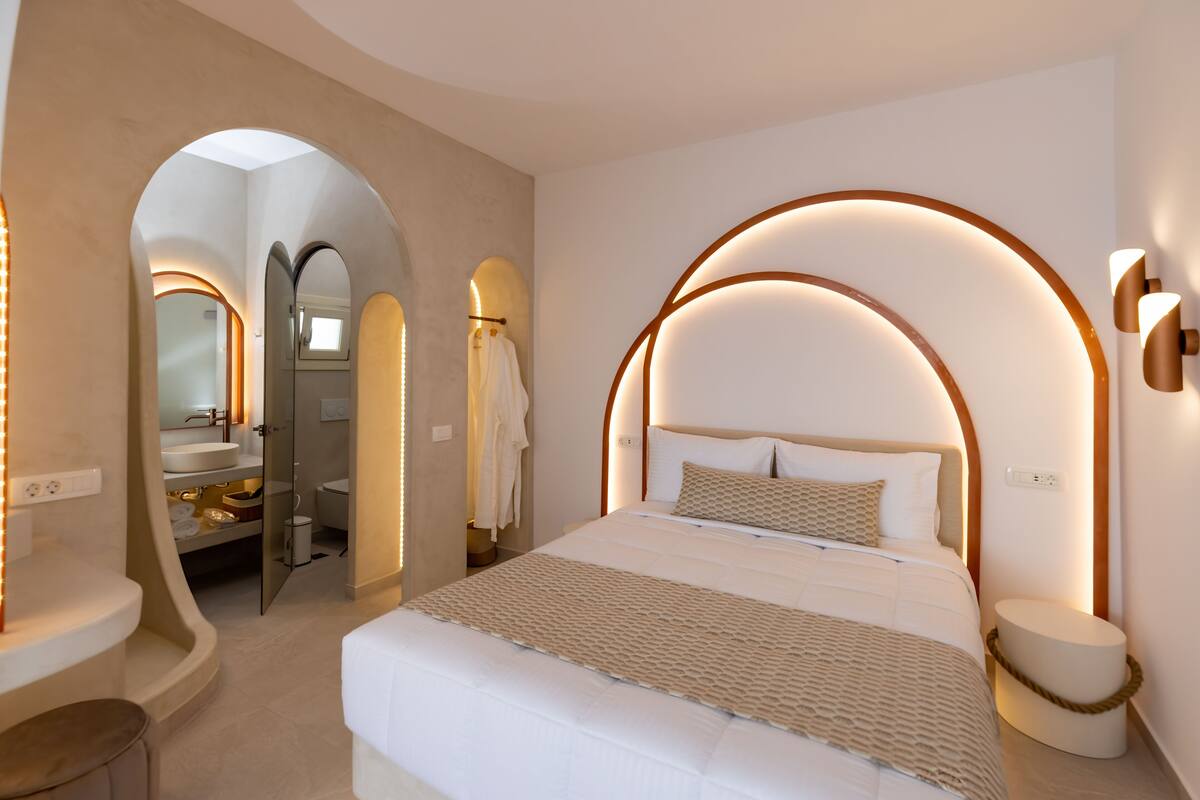 A modern bedroom with a large bed, a vanity with a mirror, and a bathroom visible through an archway.