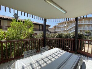 A covered outdoor area with a table and benches, surrounded by a fence and greenery.