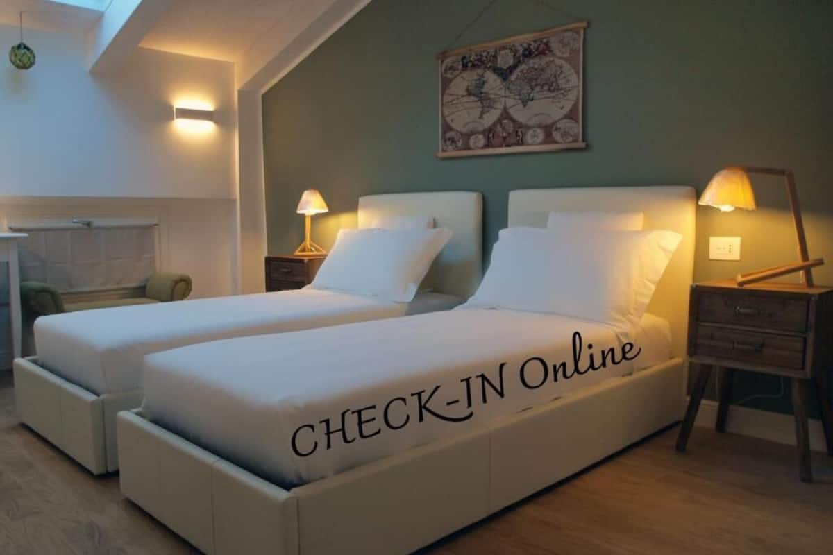 A double bed with a "CHECK-IN Online" sign, two bedside lamps, a wall clock, and a decorative piece above the bed.