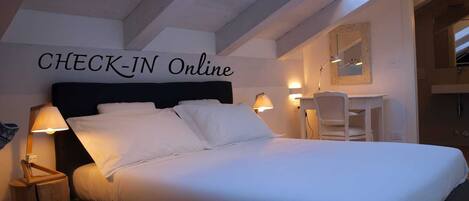 Una habitación de hotel con una cama, lámparas de noche, un escritorio y un espejo. La pared tiene un cartel que dice "CHECK-IN Online".
