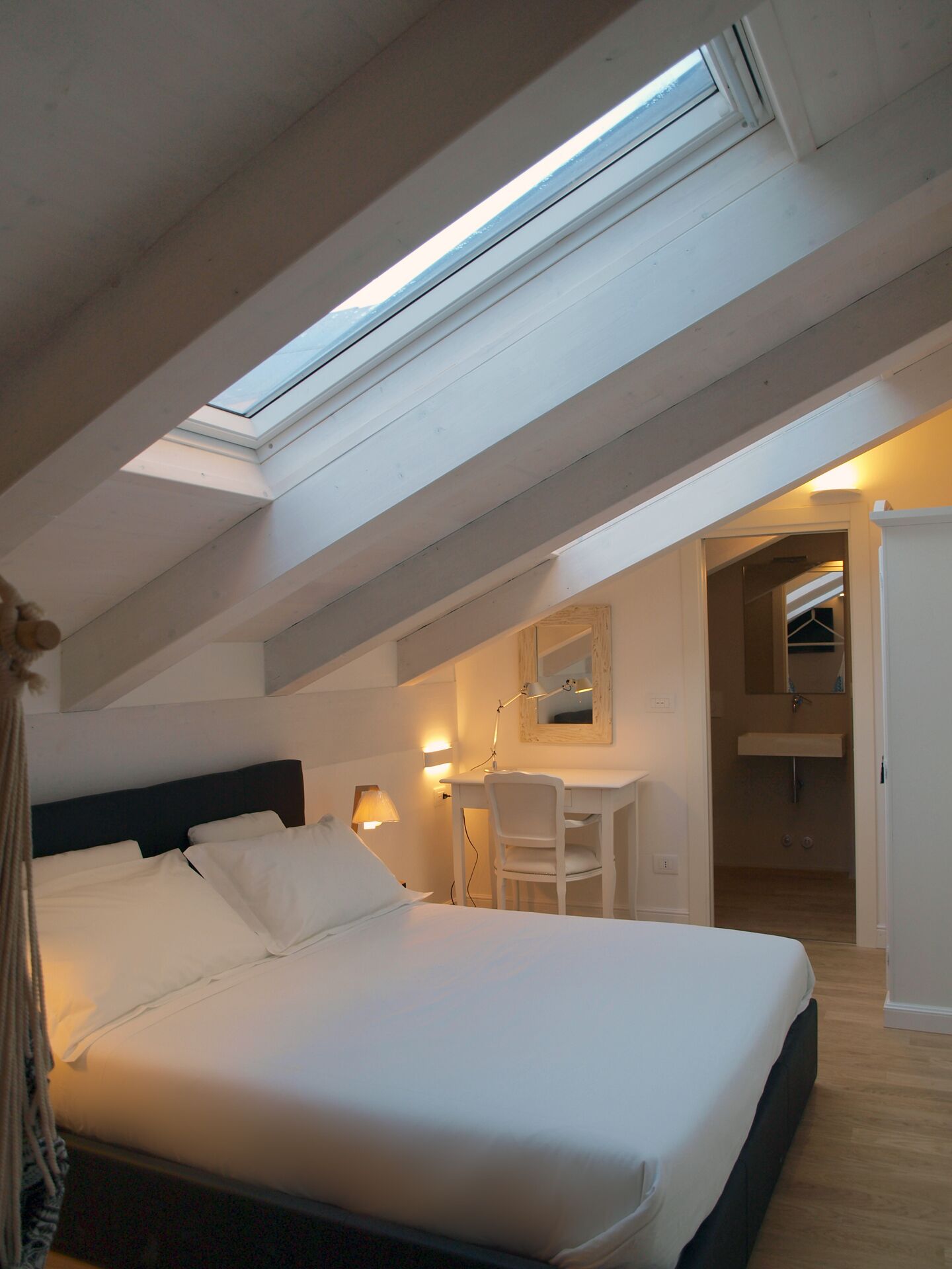 A bedroom with a skylight, a bed, a desk, and a mirror.