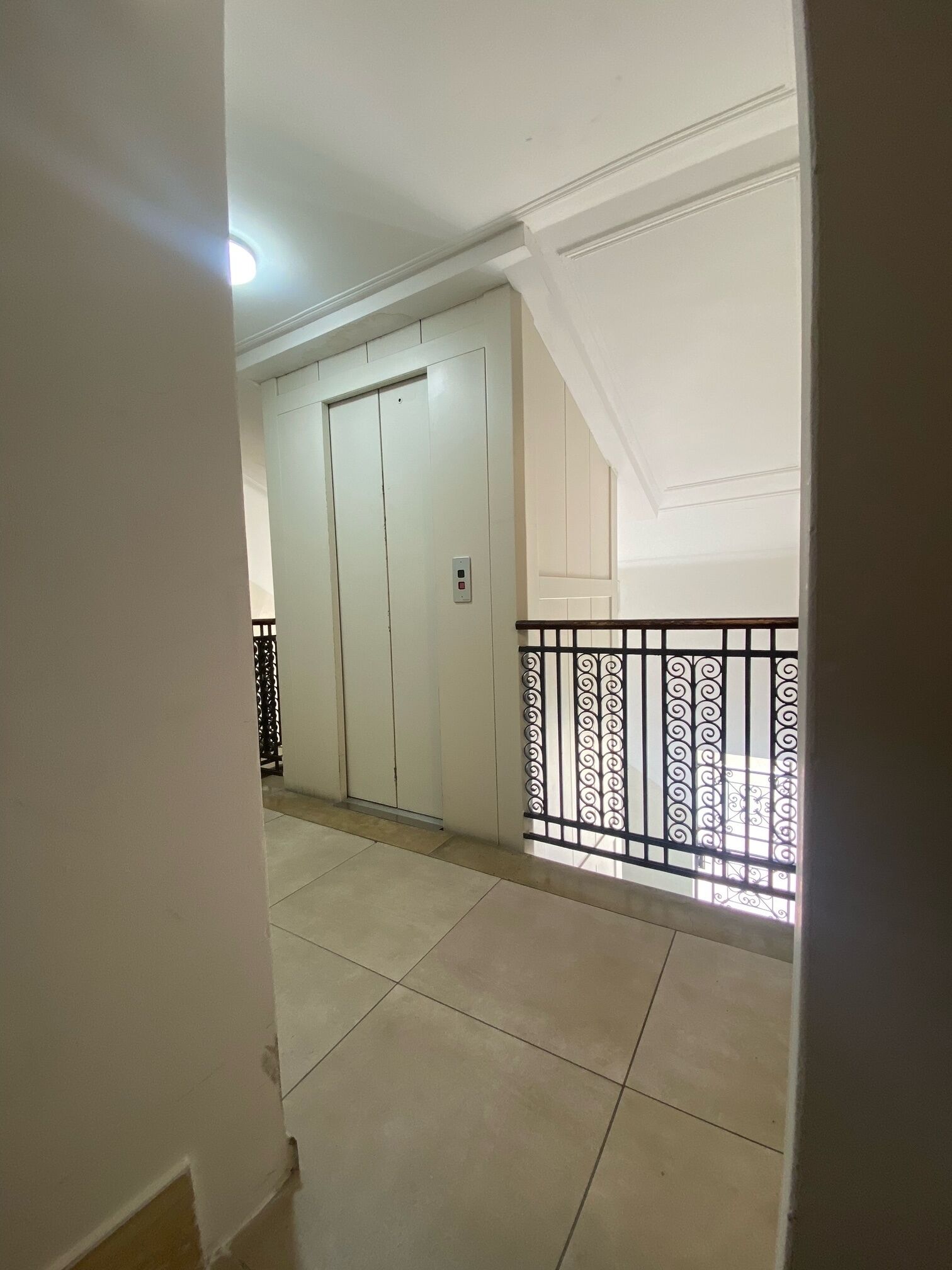 A corridor with a white door, a metal railing, and a tiled floor.