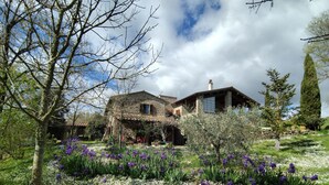 Une maison en pierre avec un jardin rempli de fleurs et un ciel dégagé.