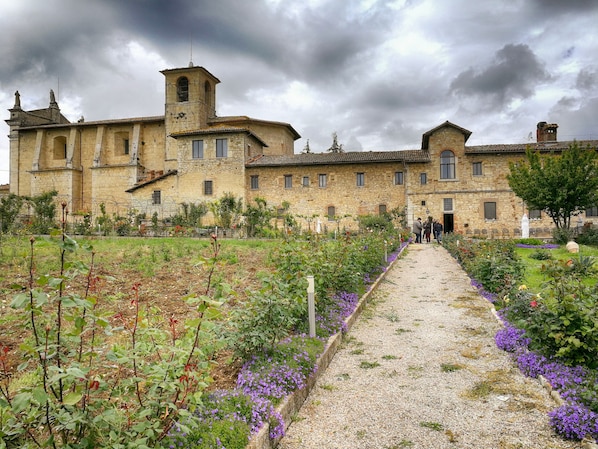 A historic stone building with a central tower, surrounded by a gravel pathway and flower beds. - Agriturismo Casa Greppo - Il Mandorlo (San Venanzo)