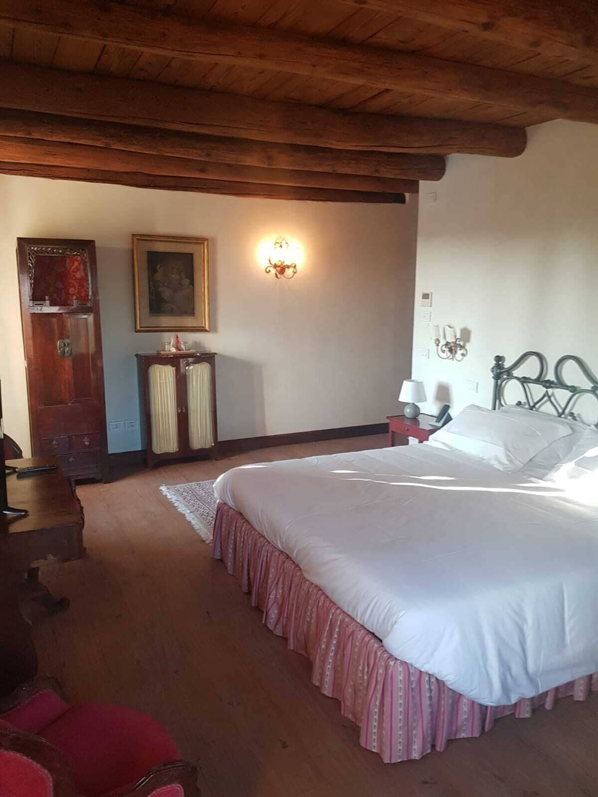 Un dormitorio con una cama grande, techo de madera, cómoda, una silla y un cuadro en la pared.