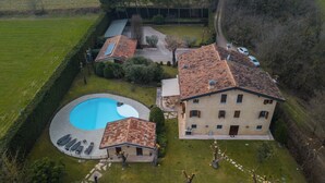 An aerial view of a property with a swimming pool, a large building with a tiled roof, and a well-maintained lawn.