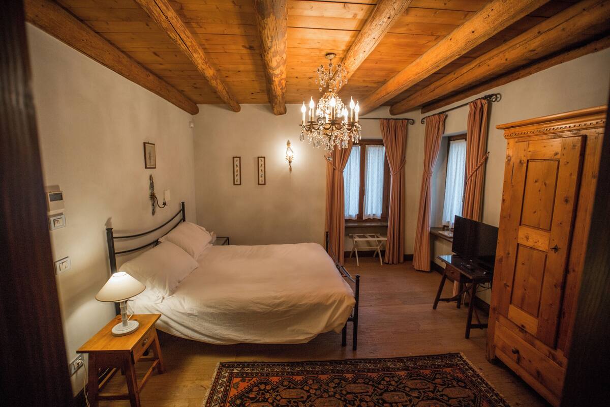A bedroom with a wooden ceiling, a bed, a desk, a television, and a wardrobe.