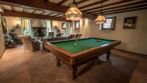 A pool table in a room with wooden beams, a fireplace, and a sofa.