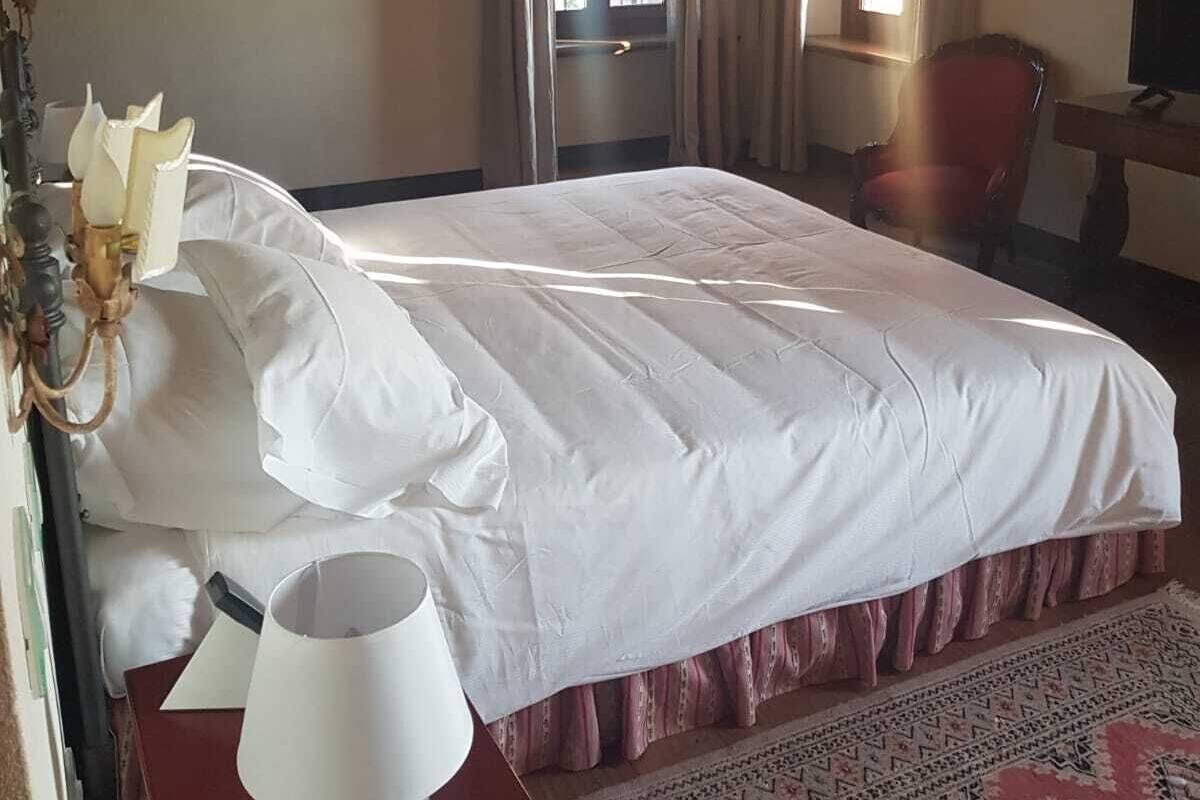 A bedroom with a bed, a chair, a desk with a lamp, and a window with curtains.