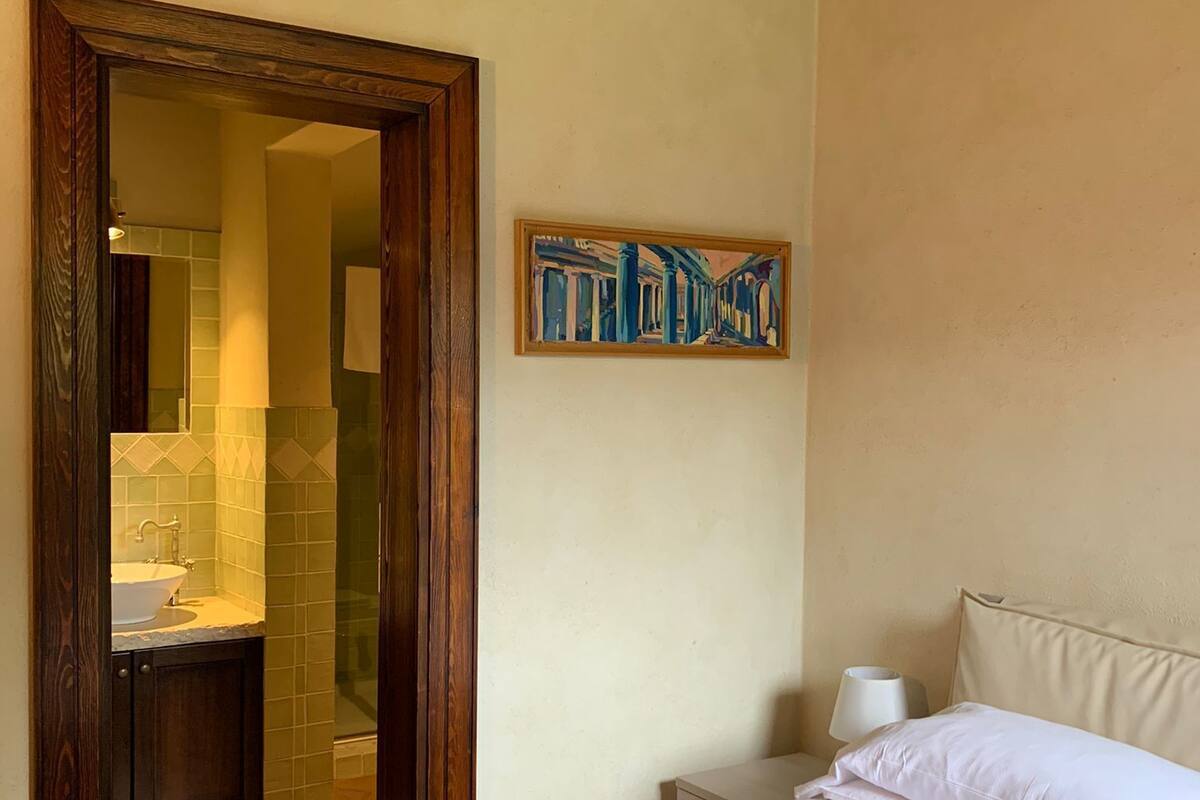 A bedroom with a wooden ceiling, a bed with white bedding, a nightstand with a lamp, and a painting on the wall.