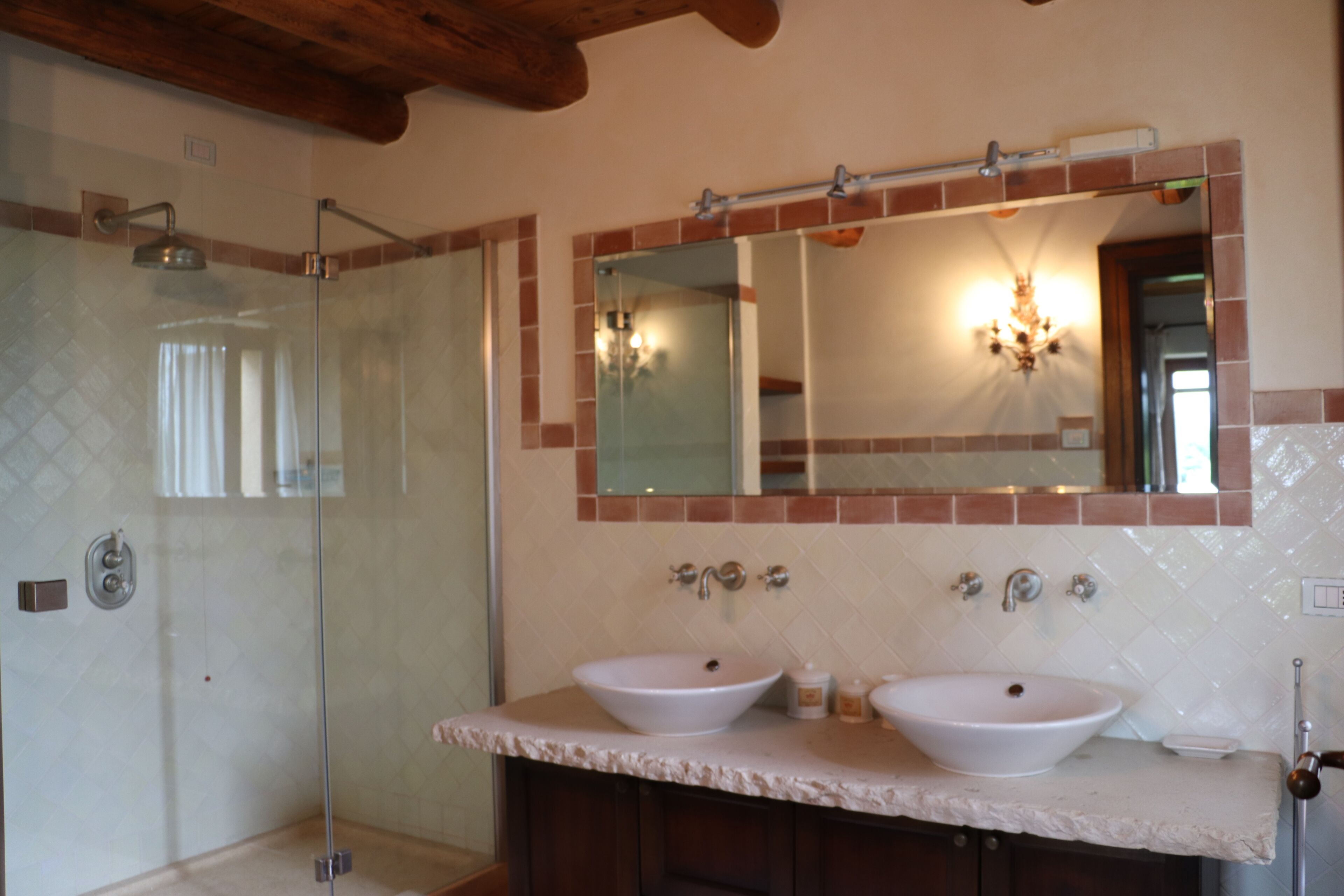 A bathroom with a glass-enclosed shower, two sinks, and a large mirror with a light fixture above it.