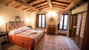 A bedroom with a wooden ceiling, a bed with a floral bedspread, a nightstand, a dresser, and a window with curtains.