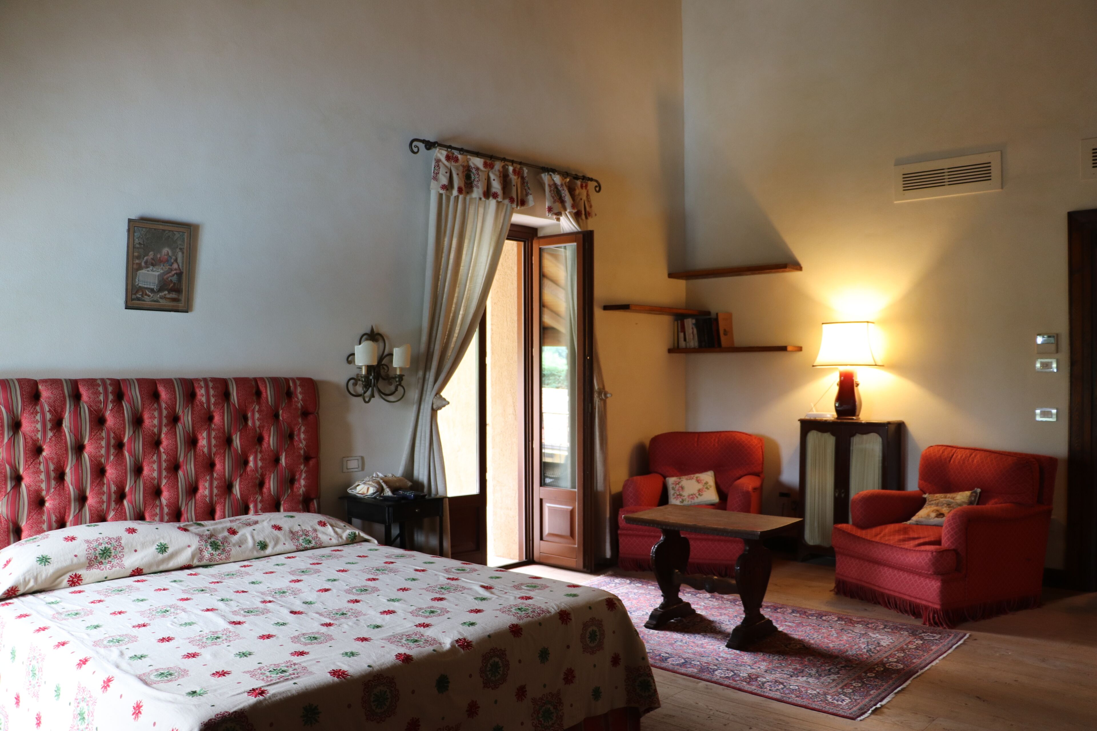 A hotel room with a bed, a red upholstered chair, a small table, and a lamp.