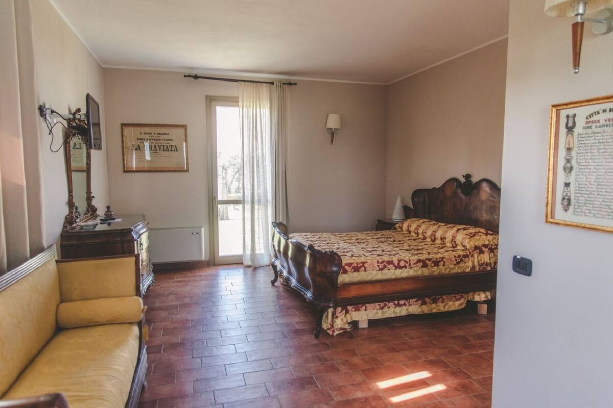 A bedroom with a bed, a chair, a dresser, and a window with curtains.