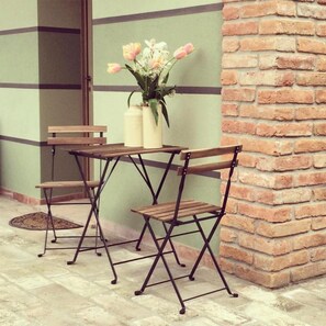 A small outdoor seating area with a brick wall, a table, and two chairs. - Agriturismo Bassanine (Monticelli d'Ongina)