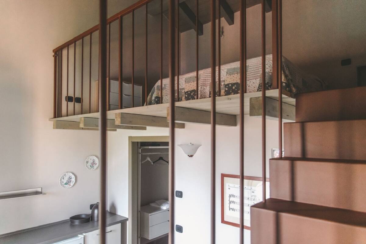 A staircase with a wooden railing leading to a loft bedroom with a patterned bedspread.