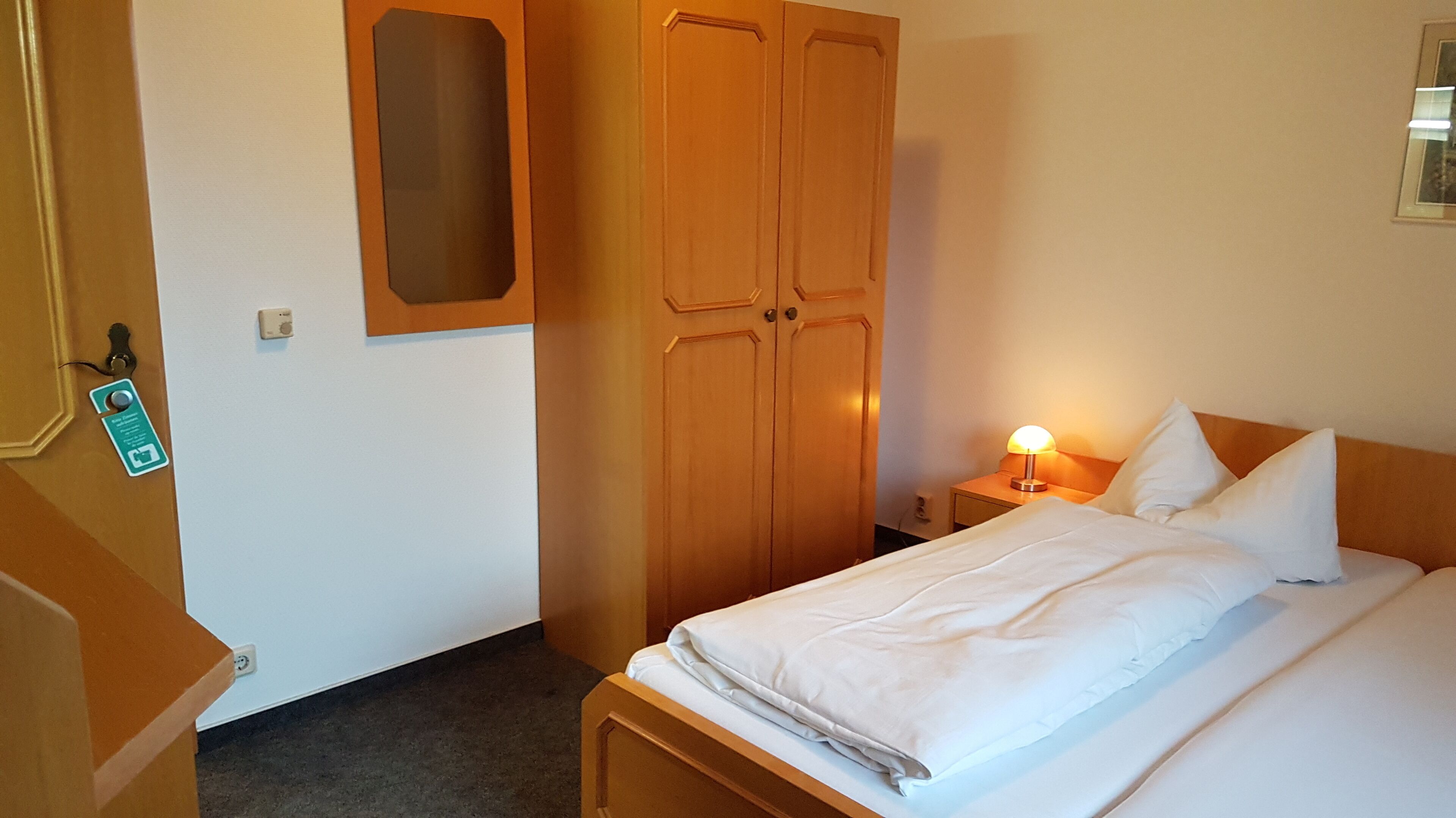 Une chambre d’hôtel comprenant un lit, une table de chevet avec une lampe, une armoire et une porte dotée d’un lecteur de carte magnétique.