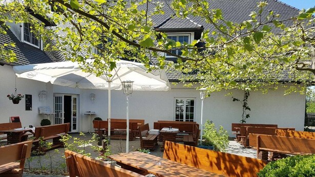 Ein Straßencafé mit Holzbänken und -tischen, weißen Sonnenschirmen und blühenden Blumenkörben.