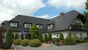 Ein traditionelles Gebäude mit einem geneigten Dach, mehreren Fenstern und einem gepflegten Garten mit verschiedenen Pflanzen und einem Weg zum Eingang.