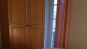 Ein Schlafzimmer mit Doppelbett, Holzschrank und einem Fenster mit Vorhängen.