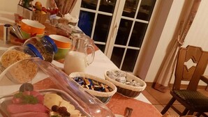 Ein reichhaltiges Buffet mit verschiedenen Speisen, darunter Fleisch, Käse und Brot, in einem Essbereich mit Blick nach draußen durch ein Fenster.