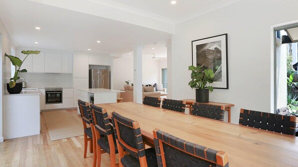 A modern kitchen with white cabinets, a built-in oven, and a dining area with a wooden table and chairs. - Byron Beachside 9 - Byron perfection (Byron Bay)
