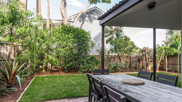 A patio with a table and chairs, surrounded by a well-maintained garden with various plants and a wooden fence.