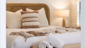 A bed with a woven headboard, multiple pillows, a bedside lamp, and a woven throw blanket.