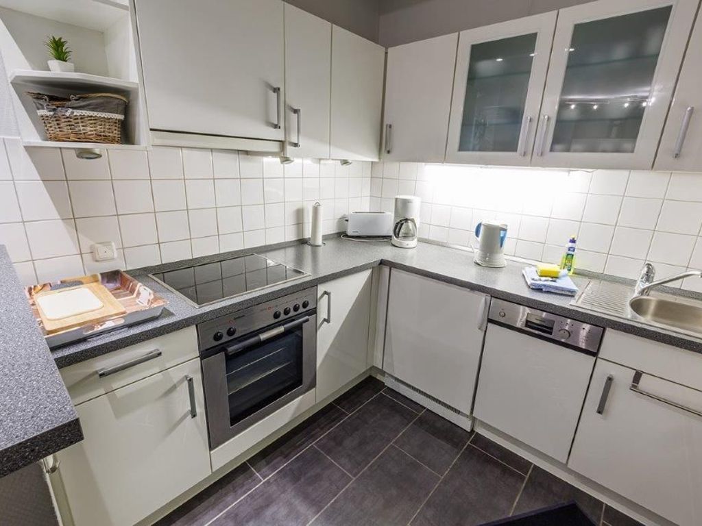 A modern kitchen with white cabinets, a built-in oven, a coffee maker, and a sink.
