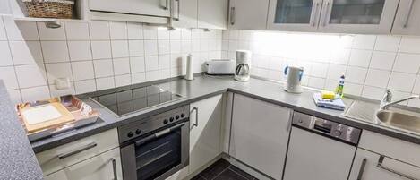 A modern kitchen with white cabinets, a built-in oven, a coffee maker, and a sink.
