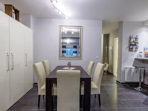A dining area with a dark wooden table and white chairs, a white cabinet to the left, and a framed mirror on the wall. - (204) 2-room apartment - Apartment house Villa Laura (Kühlungsborn)