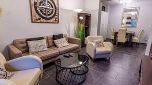 A living room with a brown sofa, two armchairs, a glass coffee table, and a dining area with a table and chairs. - (204) 2-room apartment - Apartment house Villa Laura (Kühlungsborn)
