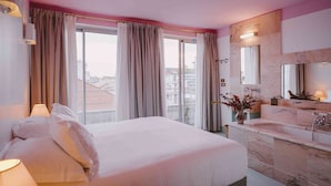 A hotel room with a large bed, a bathroom with a marble sink, and a view of the city through the window. - Hotel Amour Nice (Nice)