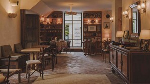A cozy dining area with a wooden table and chairs, a bookshelf with various items, and a large window providing natural light. - Hotel Amour Nice (Nice)