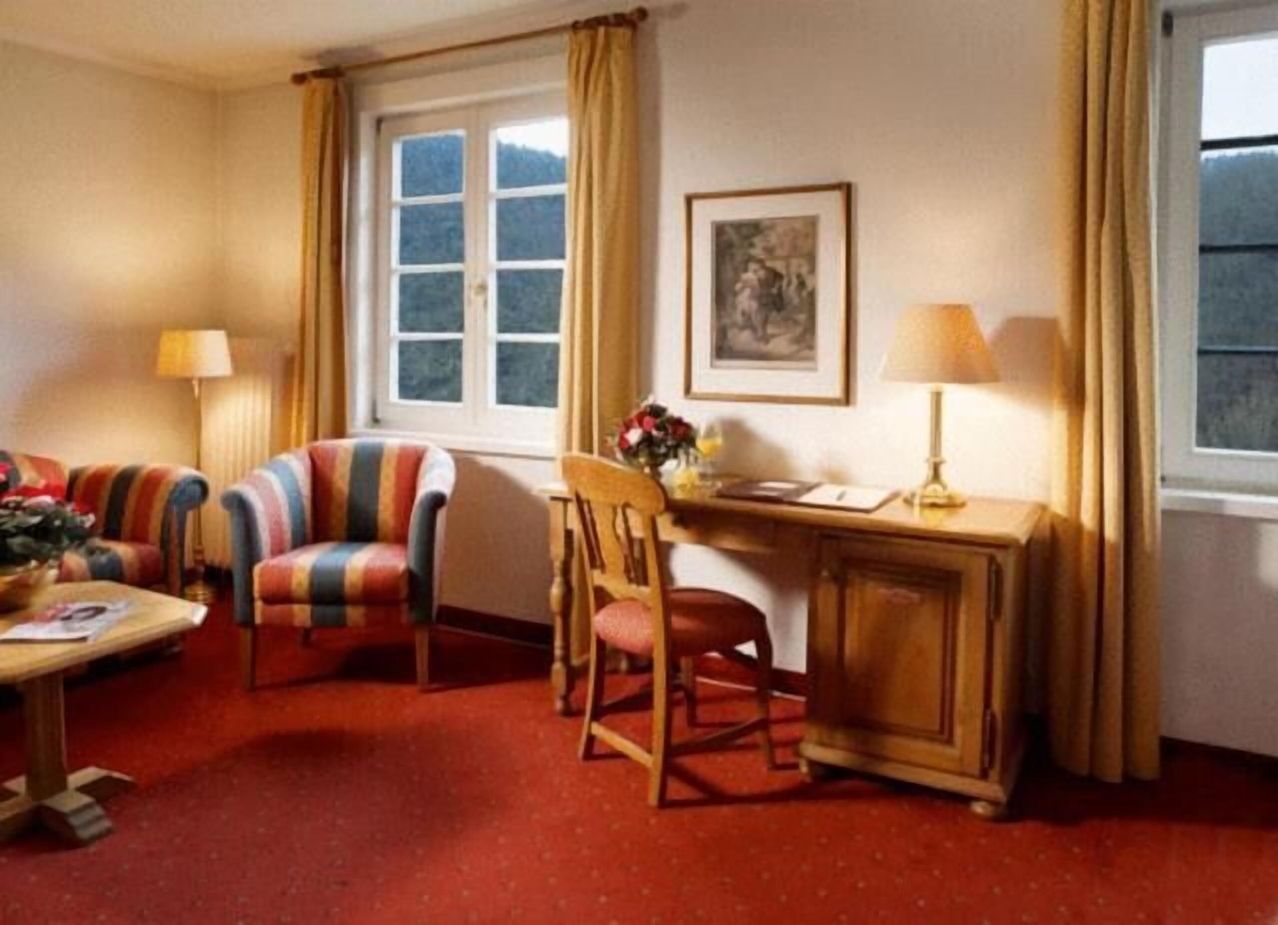 A room with a striped sofa, a wooden desk with a lamp, a chair, and a window with curtains.