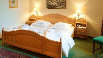 A wooden four-poster bed with white linens, two bedside tables with lamps, a framed botanical print, and a landscape painting on the wall.