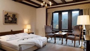A hotel room with a bed, two armchairs, a table, a chandelier, a painting, and a window with curtains. - Burghotel Schnellenberg (Attendorn)