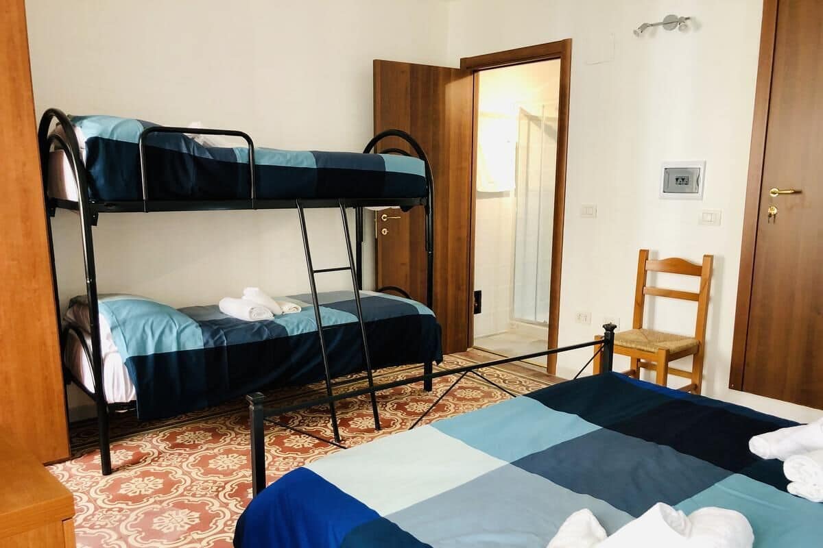 Een kamer met stapelbedden, een eenpersoonsbed, een stoel en een deur.