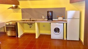A compact kitchen with a sink, stove, coffee maker, washing machine, and refrigerator. - Il Terrazzino (Iglesias)