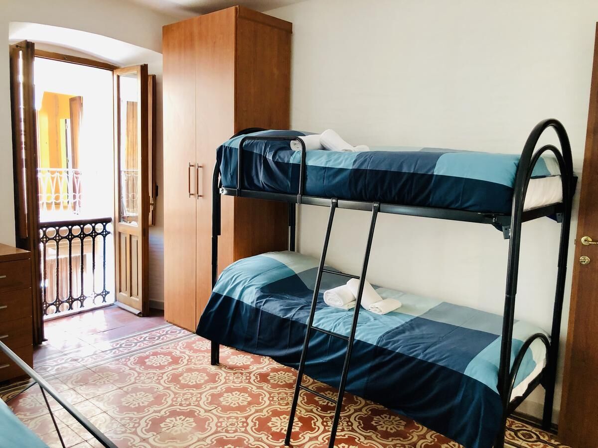 Un letto a castello con copriletto azzurro e bianco a righe, un armadio in legno e un pavimento decorato.