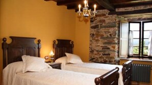 A room with two beds, a stone wall, a chandelier, and a window with a view. - Casa Rural Vila Pomar (Ribadeo)