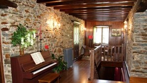 A rustic room with a wooden piano, stone walls, and a wooden staircase. - Casa Rural Vila Pomar (Ribadeo)