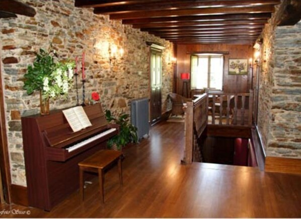 A rustic room with a wooden piano, stone walls, and a wooden staircase. - Casa Rural Vila Pomar (Ribadeo)