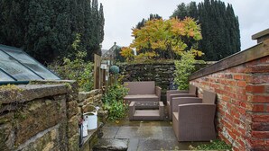 A narrow garden with a patio area, stone steps, and a brick wall. - Rosella Cottage (Pickering)
