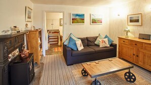 A living room with a sofa, coffee table, and a fireplace. There are framed pictures on the wall and a television on a wooden cabinet. - Rosella Cottage (Pickering)
