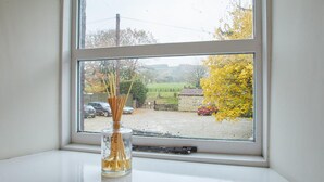 A window with a clear view of a rural landscape, including a road, parked cars, and autumn foliage. - Rosella Cottage (Pickering)