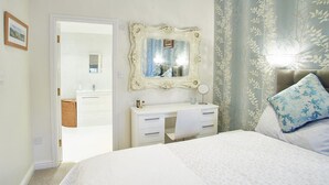 A bedroom with a bed, a dresser, a mirror, and a door leading to a bathroom. - Rosella Cottage (Pickering)