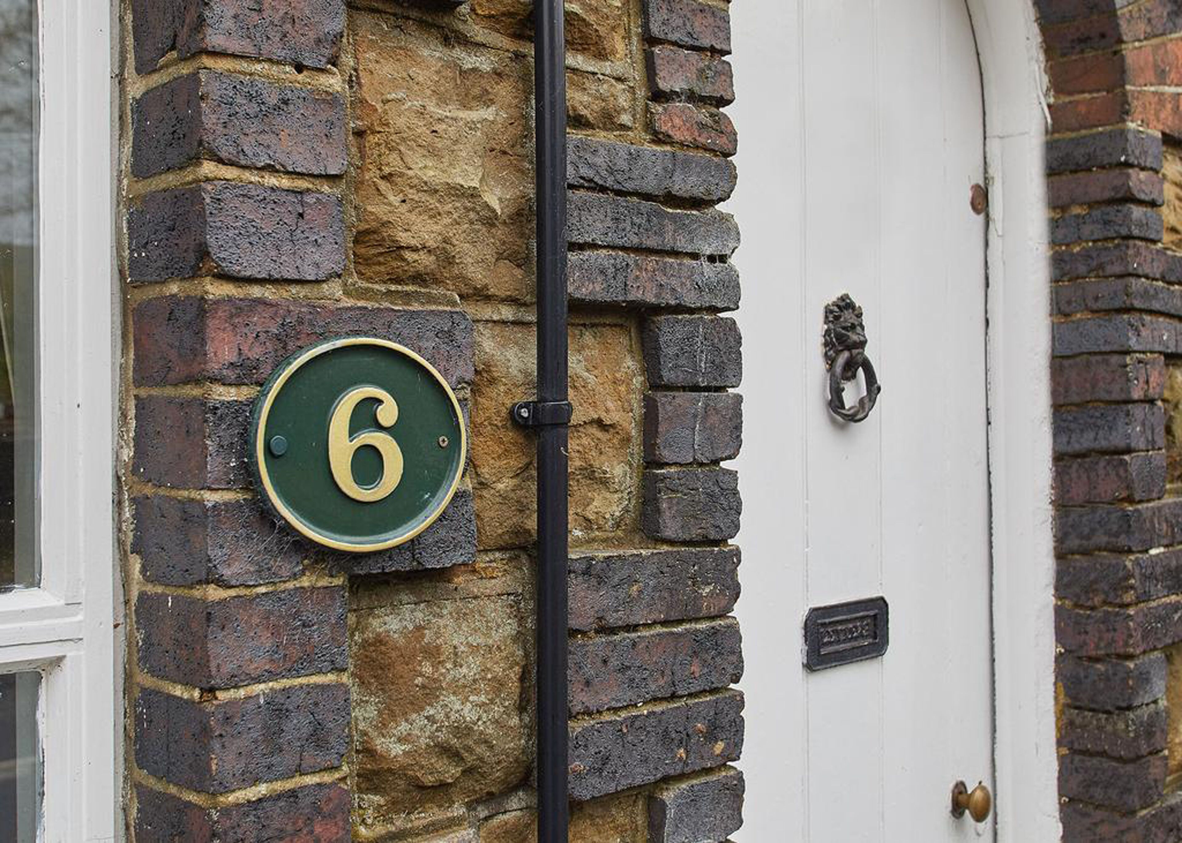 A brick wall with a green house number sign and a white door.